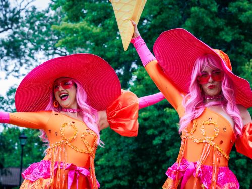 Image of two women wearing brightly-coloured clothes and wide brimmed hats, posing playfully for the camera